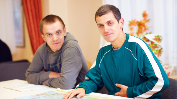 cheerful adult men with disability sitting at the desk in rehabilitation center