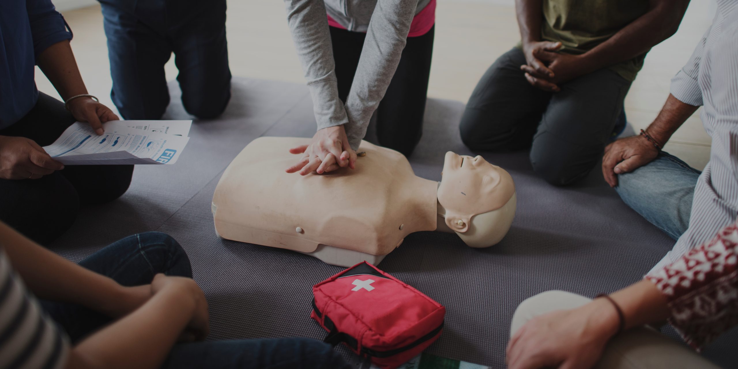 Group of people practising CPR on a training mannequin with a first aid kit nearby.