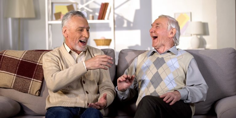 Two elderly men laughing together on a sofa.