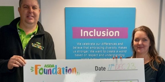 Rebecca Smicle, CEO of Independent Lives receives grant from ASDA Foundation holding a cheque with the word 'Inclusion' in the background.