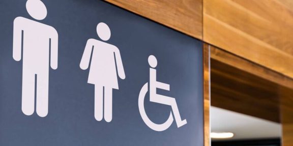 Accessible toilet sign with icons for male, female, and wheelchair users.